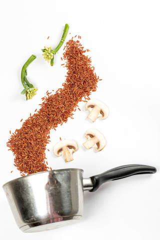 Cooking concept, brown rice, mushrooms and broccolini scattered on white background with ladle