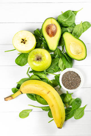 Fresh avocado, apples, spinach leaves and chia seeds on a white wooden background, top view