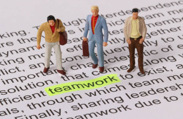 Group of miniature man standing next to a word teamwork highlighted in yellow