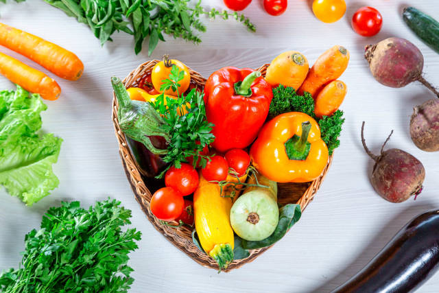 Fresh vegetables in the basket and around it on a white wooden background. Top view