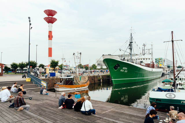 People seating on the embarkment at the Bremerhaven port with big and small ships parked