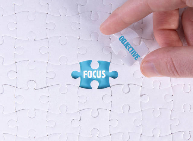 Hand holding piece of jigsaw puzzle with word focus & objective