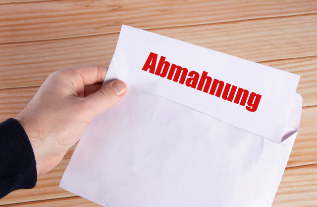 Hand holding open envelope with Abmahnung text