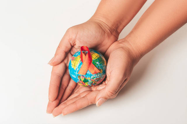 World Aids Day Concept. Hands holding globe with AID red ribbon