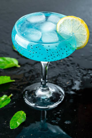 Cold blue cocktail with ice,lemon slice and mint leaves on black background
