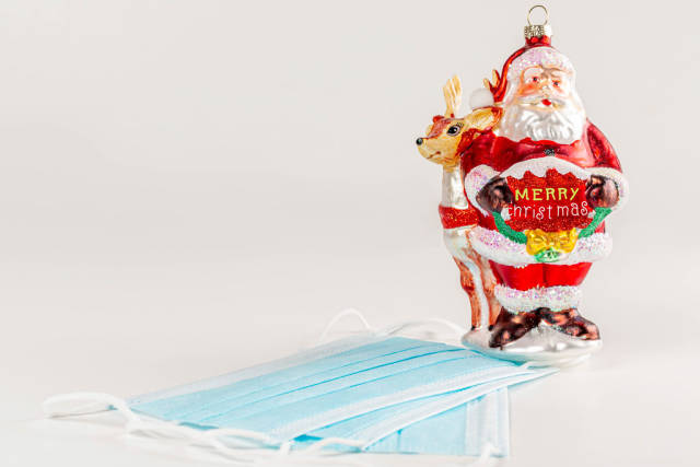 Toy santa claus holding a wish of merry christmas in his hands on a white background with medical masks