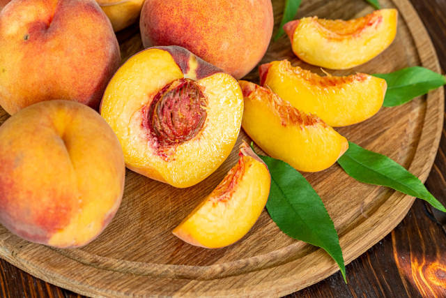 Whole and sliced fresh peaches on a wooden background with leaves
