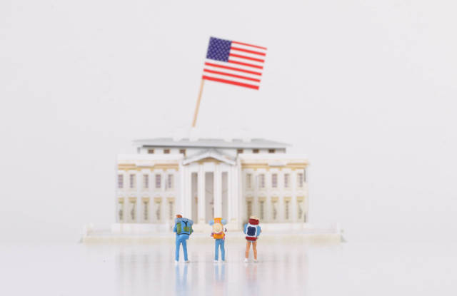 Miniature travelers stading in front of the White House with USA flag