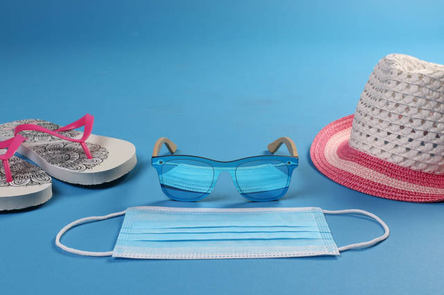 Medical face mask with sun hat, flipflops and sunglasses on blue background