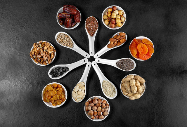 Dried fruits, nuts and seeds in spoons and bowls on a black background. Top view