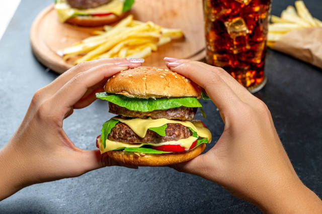 A woman holding a large hamburger on the background of fast food