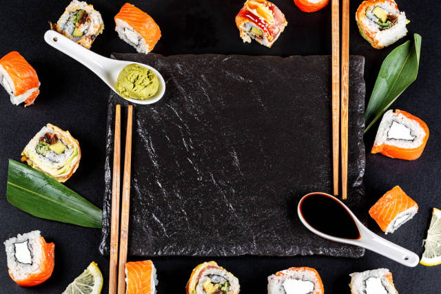 Japanese food frame with different sushi, sauces and chopsticks on black background, top view