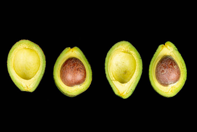 Fresh avocado halves with and without seeds on black background, top view
