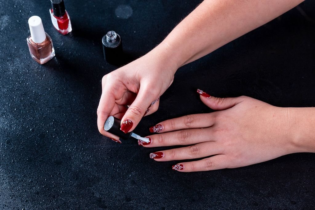Frau lackiert ihre Fingernägel mit rotem Nagellack und festlichen Zeichnungen auf dunklem Tisch