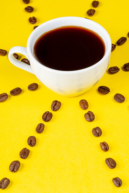 Eine Tasse-frischer Kaffee auf gelbem Hintergrund mit Kaffeebohnen