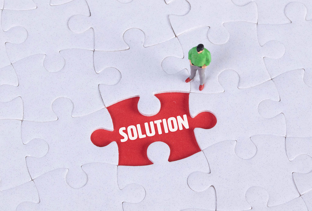 Miniature man looking at a missing puzzle piece with Solution text