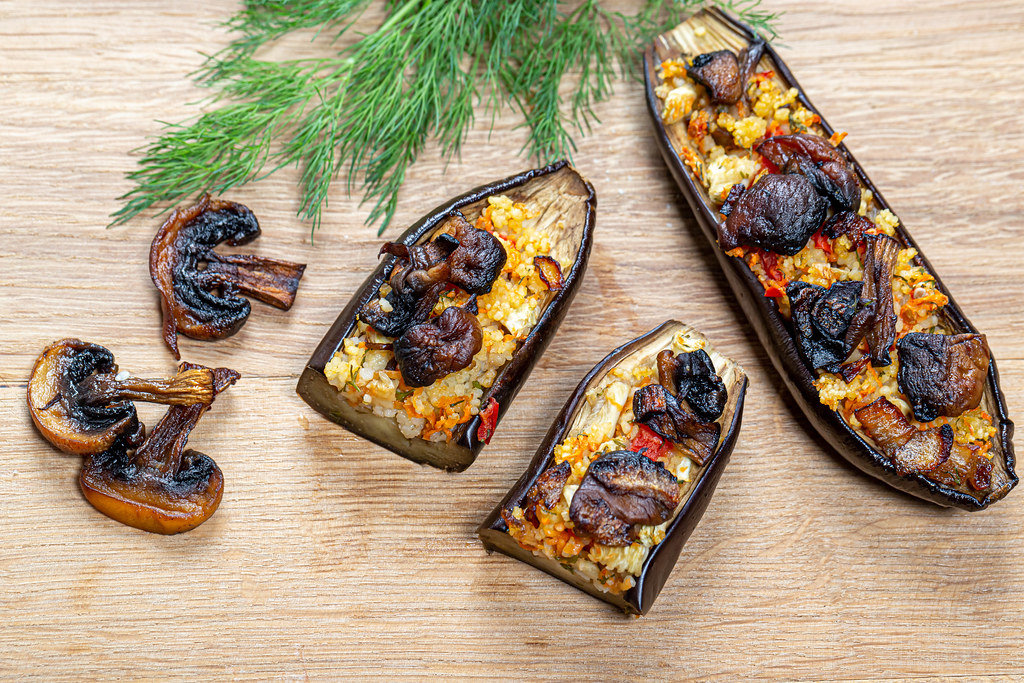 Baked eggplant with vegetables, couscous and mushrooms on a wooden background. Top view