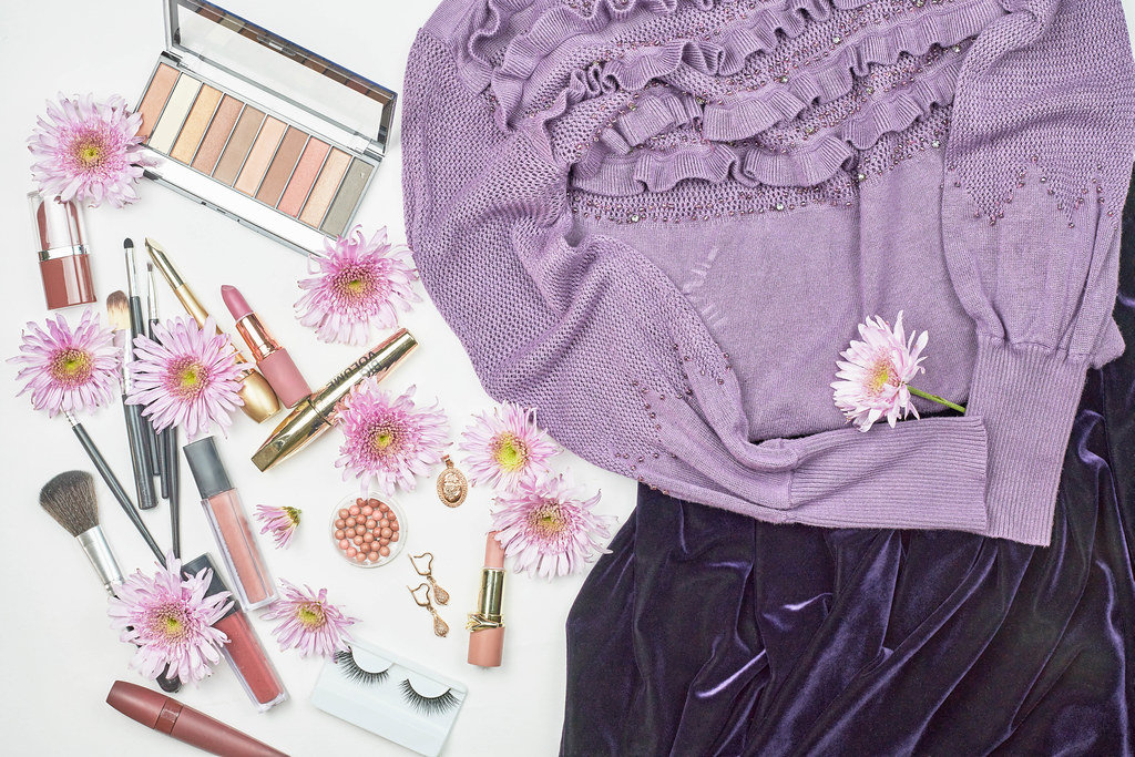 Violet colored light sweater and skirt with make-up tools and spring flowers
