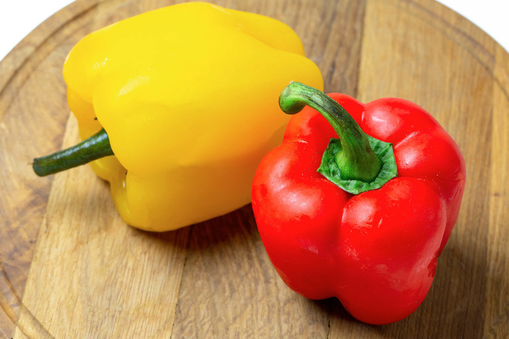 Yellow and red fresh bell peppers on a wooden kitchen board