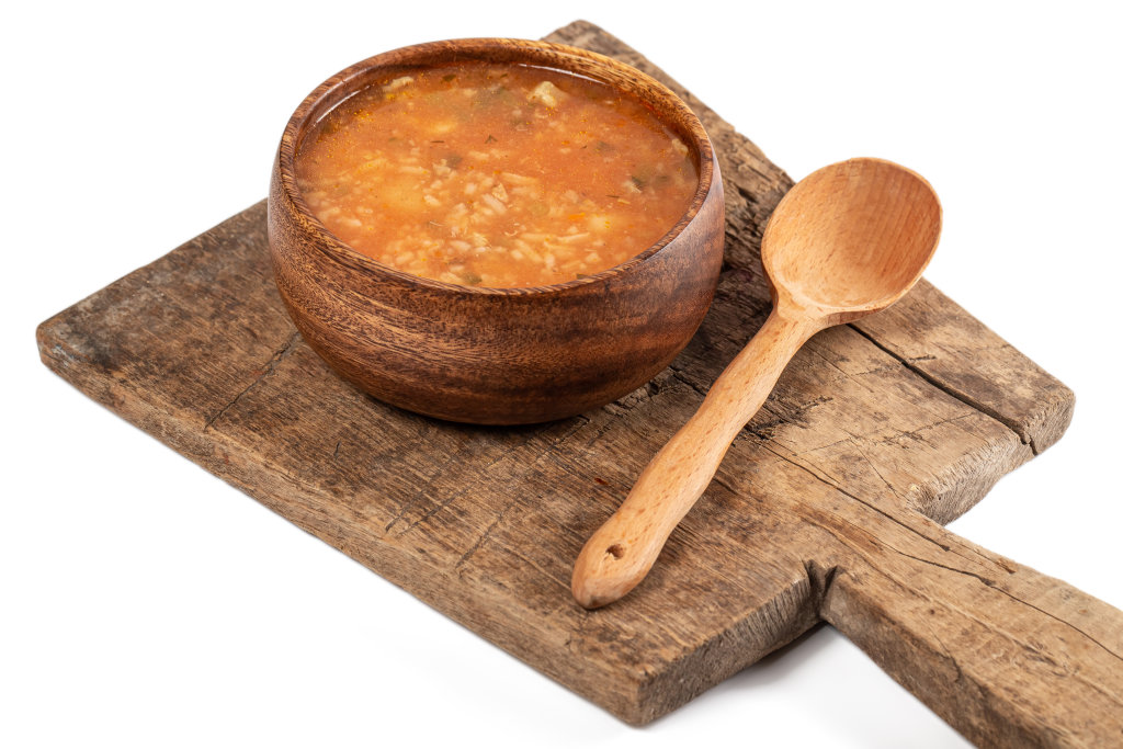 Wooden bowl of soup with rice, meat, tomatoes and pickles on an