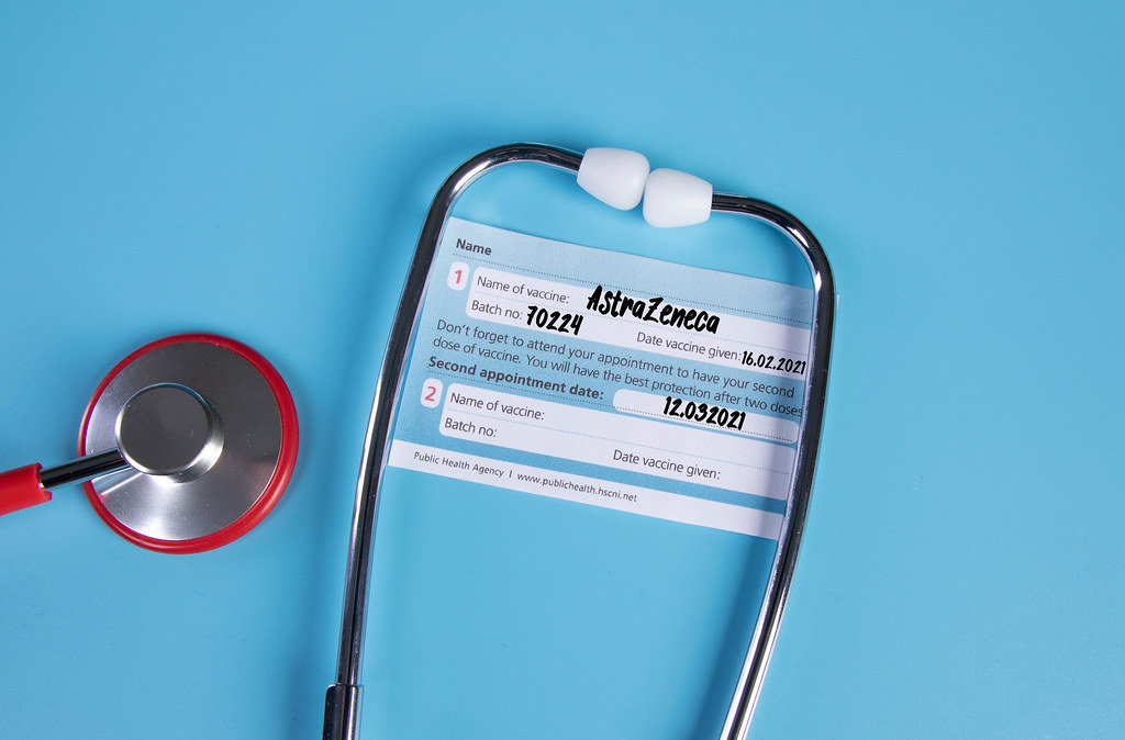 Stethoscope with AstraZeneca Covid-19 vaccination certificate on blue background