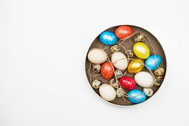 Dyed and non-dyed easter eggs and quail eggs on a plate, top view on white background with copy space