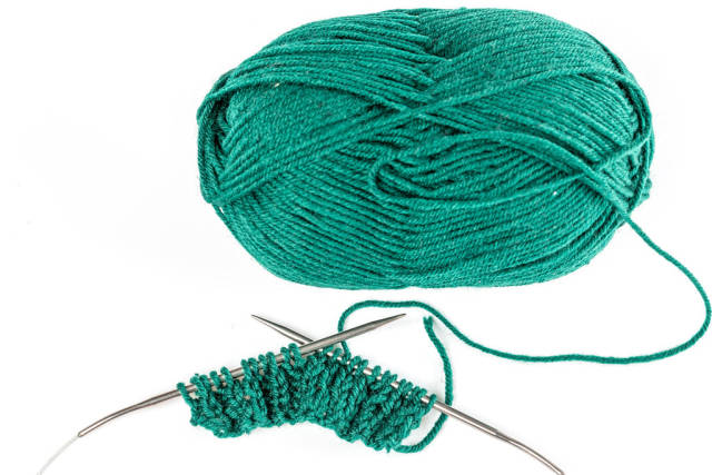Top view, ball of green yarn with knitting needles