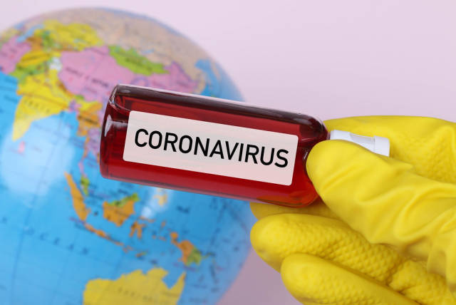 Hand holding blood sample in test tube with Coronavirus text and globe in the background