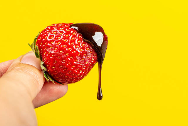 Chocolate drips from fresh strawberries on a yellow background