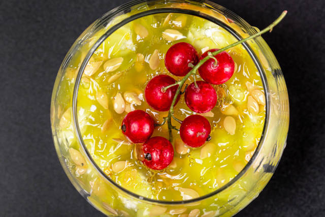 Top view, a sprig of red currant on the pulp of a Kiwano fruit with seeds in a glass