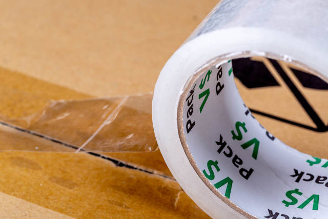 Close-up roll of adhesive tape on cardboard box. The concept of packing or sending