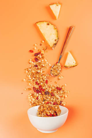 Top view, bowl, oatmeal with berries, seeds and pineapple slices on orange background