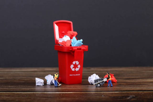 Paper in red recycle bin with tiny cleaning workers