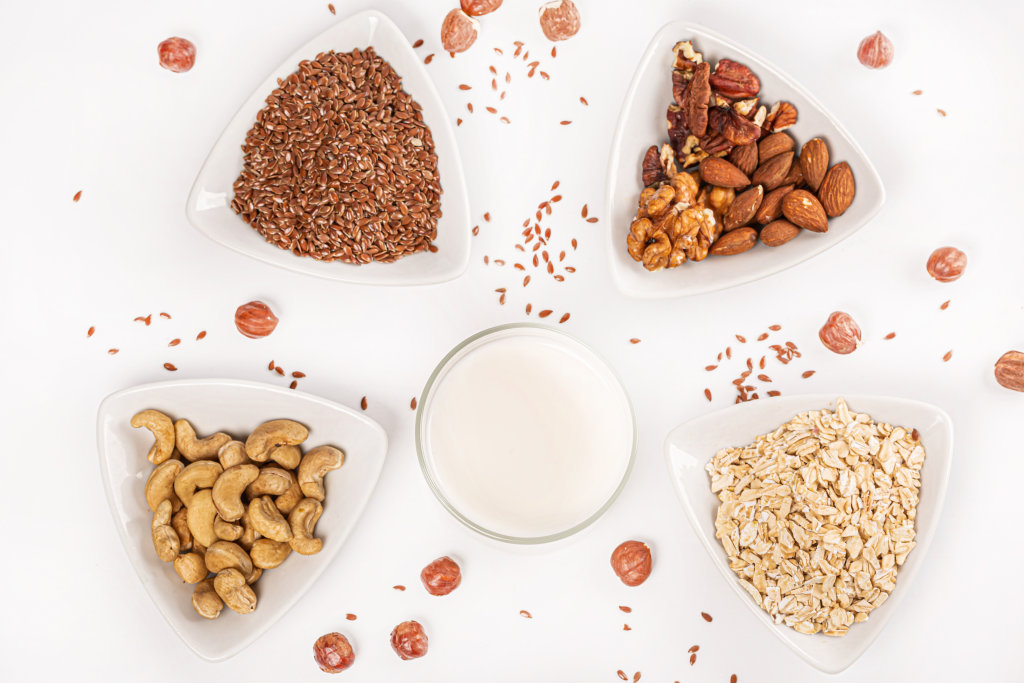 Glass of milk with nuts and seeds in triangular bowls, top view