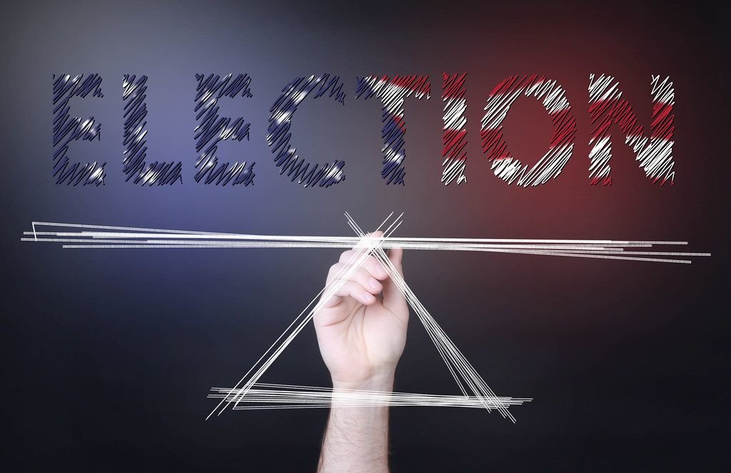 Eine Person zeichnet eine Waage unter dem Text Election in Farben der US-Flagge