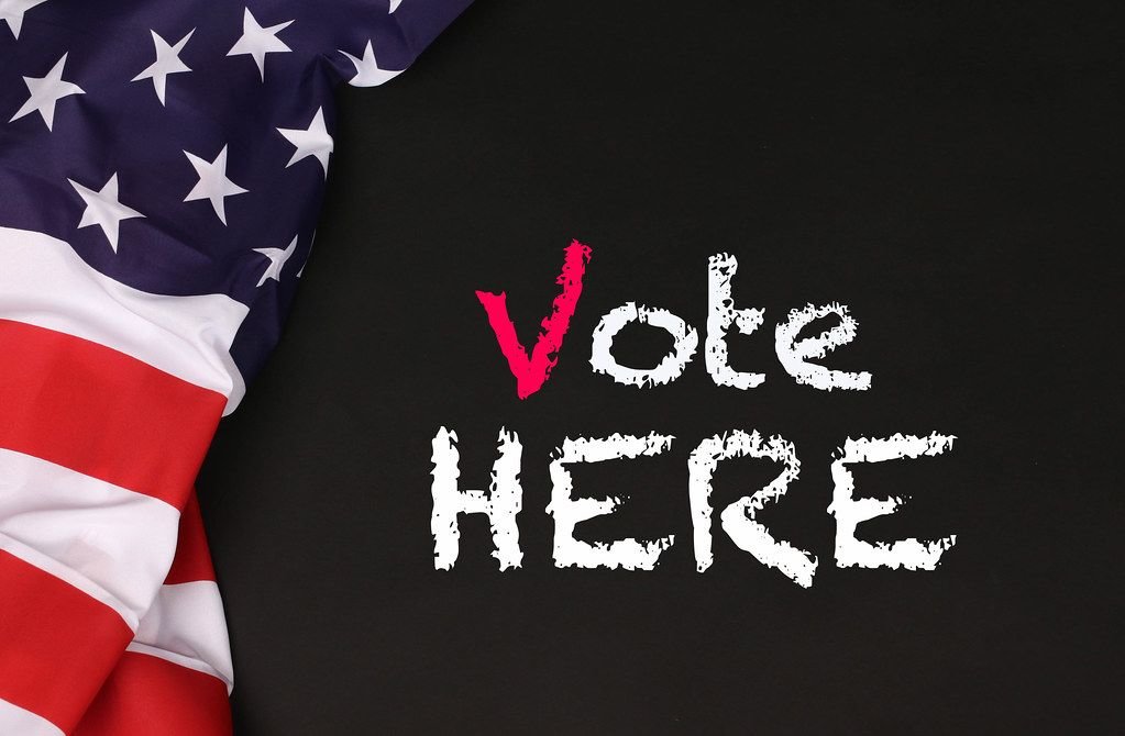 Amerikanische Flagge mit Text Vote Here auf schwarzem Hintergrund