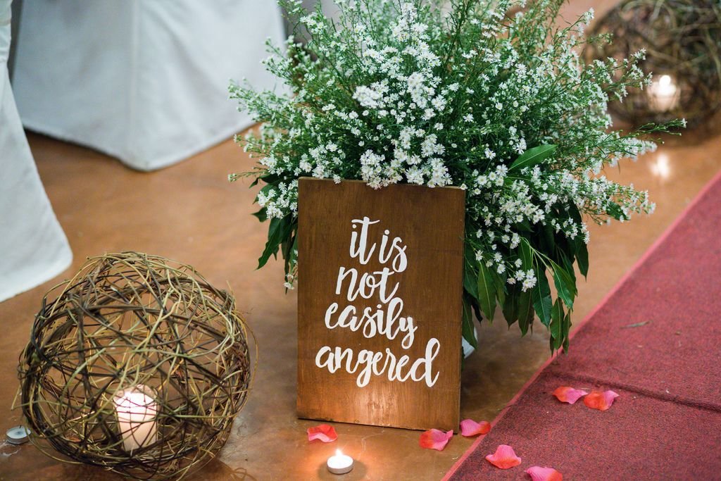 Dekoration mit weißem Blumenstrauß, Kerze in Strohkugel und Holztafel mit Zitat auf Boden