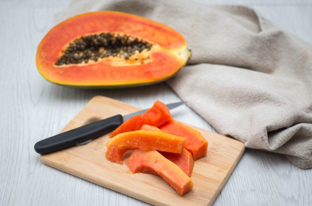 Geschnittene Papaya auf einem Brettchen mit Messer und Papaya-Frucht im Hintergrund