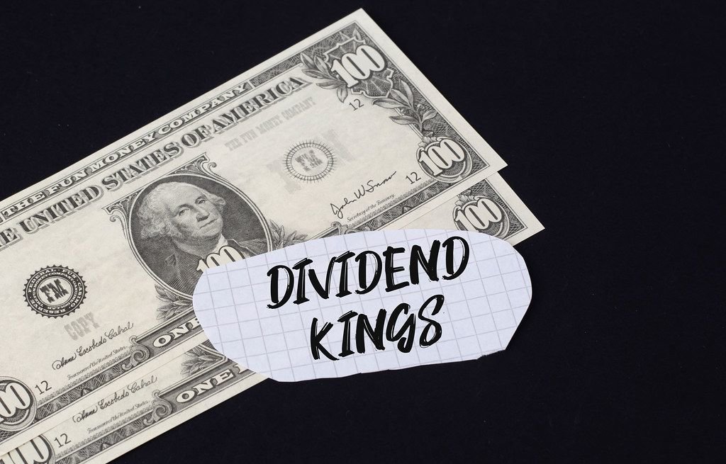Dividend kings" Text auf kariertem Zettel mit zwei 100-Dollar-Scheinen vor schwarzem Hintergrund