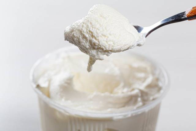 Saure Sahne in einem Plastikbecher und auf einem Löffel