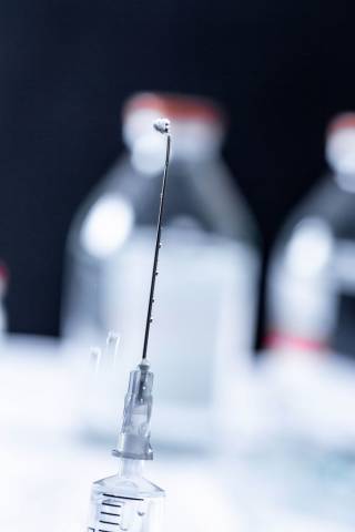 Nahaufnahme von Spritzennadel mit Tropfen von Medizin an der Spitze