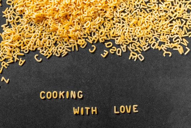 Cooking with Love aus Buchstaben-Pasta auf schwarzem Hintergrund