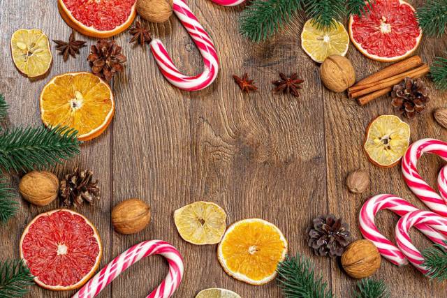 Obene Aufnahme von Weihnachtslutscher mit getrockneten Zitrusfrüchten und Tannenzweigen auf einem Holztisch