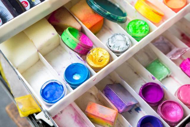 Set aus Theaterschminke mit Schwämmen und Farbtöpfen in blau, gelb, grün und pink in weißer Plastikbox
