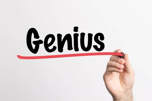 Hand schreibt das Wort "Genie / Genialität" auf ein Whiteboard