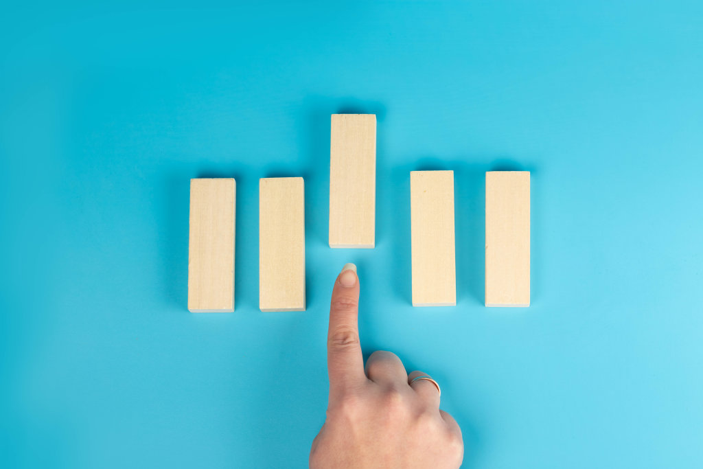 Choice concept, finger points to wooden block in front, blue background, top view