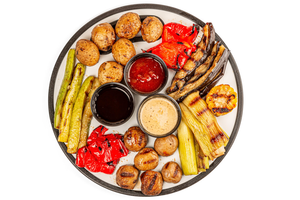 Top view, fresh grilled vegetables and mushrooms with three sauces on a round kitchen board