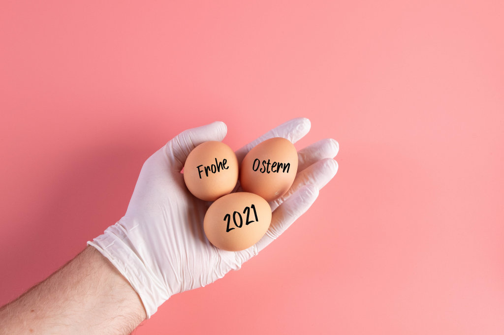 Hand in protective gloves holding eggs with Frohe Ostern 2021 text