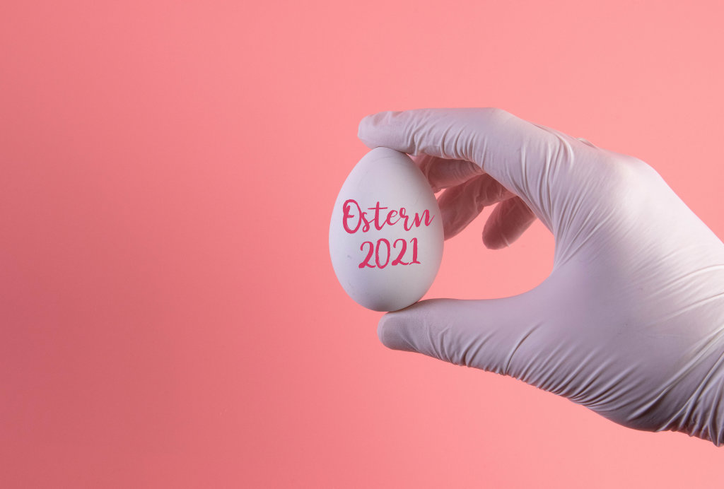 Hand in protective gloves holding white egg with Easter 2021 text