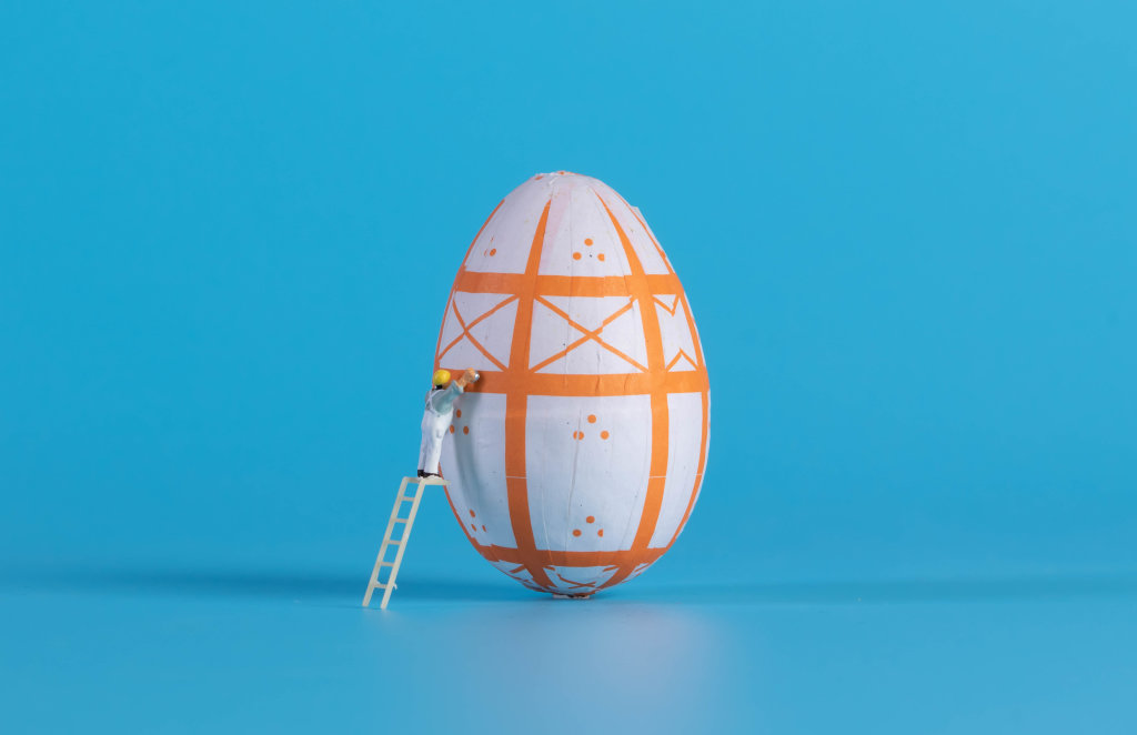 Miniature painter painting easter egg on blue background